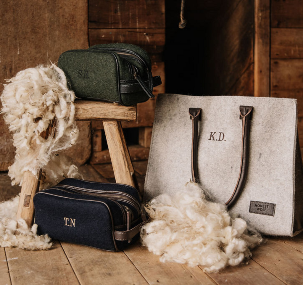 Two Honest Wolf Washbags with embroidered initials on a wooden floor with wool fibers sitting alongside an Honest Wolf Casual Shopper